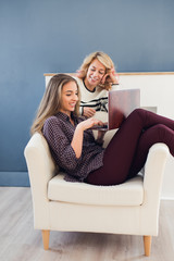 Two happy young woman using laptop at home