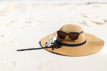 Glasses and a hat with frangipani flower on the beach.