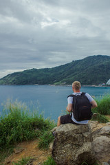 Traveller sitting near the ocean. Back view of a traveller sitting and looking at the seascape. Vertical outdoors shot.