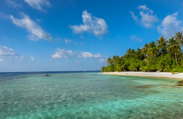 Landscape of a tropical  blue turquoise crystal clear ocean water and sandy beach in Maldives island. Blue cloudy sky in the background.