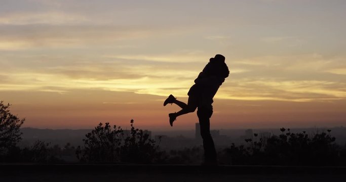 Man lifts woman, romantic sunset silhouette