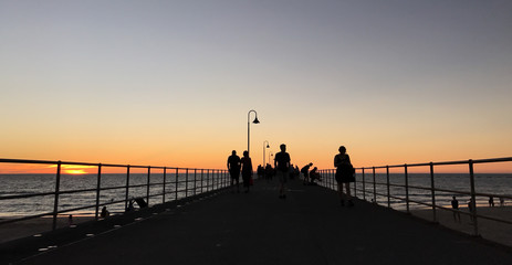 Friends in silhouette walking along pier at sunset