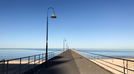 Lamp posts on empty pier stretching out into sea on clear summer day