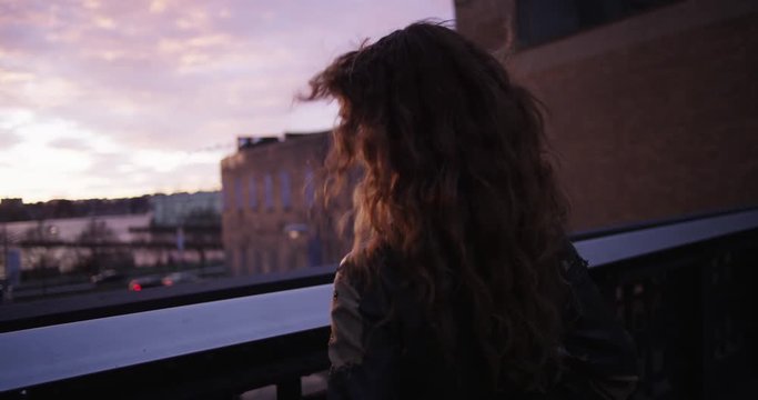 Young woman walks up to balcony, sunset