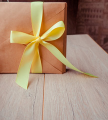 Kraft envelope tied with a yellow ribbon on a wooden background. Homemade gift envelope with yellow ribbon