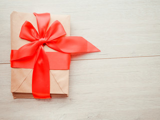 Kraft envelope tied with a red ribbon on a wooden background. Homemade gift envelope with red ribbon