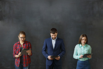 Three people - one man and two girls are standing at the wall with tablets.