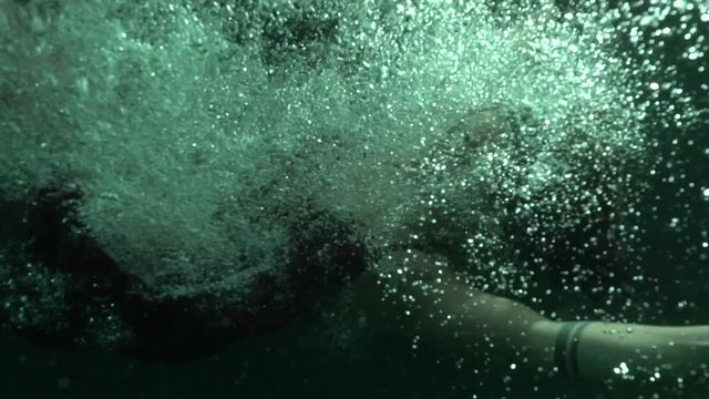 Woman jumps underwater at night, slow motion