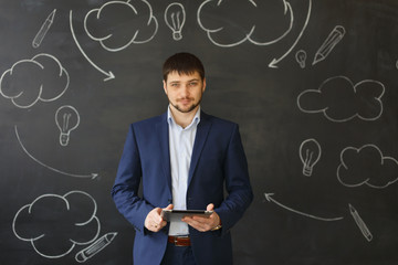 Successful businessman standing using a tablet to access the internet as he leans against a white wall with copyspace