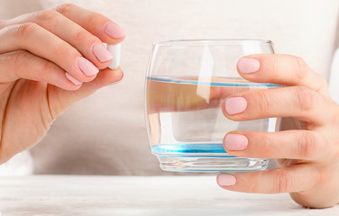 Woman holding glass of water and pill.