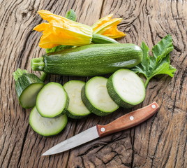 Zucchini with slices and zucchini flowers on a wooden table.