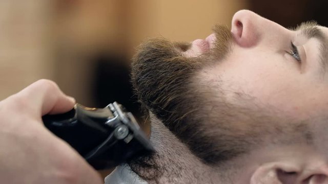 Horizontal portrait of a barber shaping beard of his client using a trimmer