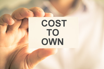 Businessman holding COST TO OWN message card