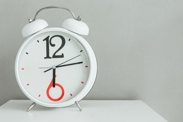 Interesting analog white clock with arrows and big figures stand against a gray wall background