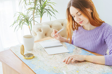 Happy travel planing woman with map, notebook , toy airplane, compass and cup of tea. Sunny light room. 
