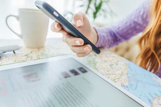 Phone in woman hands. Tablet opened on-line site. Cup of tea. Close up. Map on the table. 