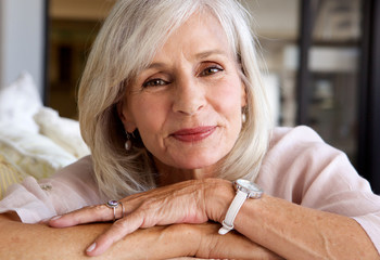 relaxed older woman smiling and sitting on sofa