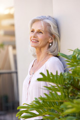older woman leaning on wall outside smiling