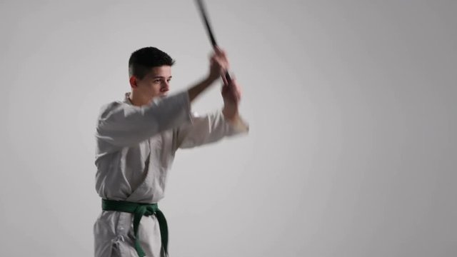 Katana usage at a workout of a young sportsman in white kimono in studio