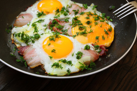 Fried eggs with bacon in a frying pan and coffee on a wooden table