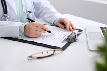 Close-up of a female doctor filling  out application form , sitting at the table in the hospital