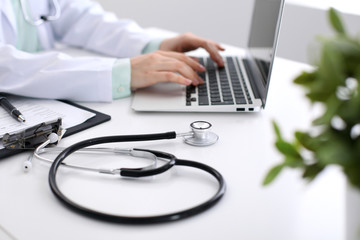 Close-up of stethoscope is lying on the table near female doctor typing on laptop computer