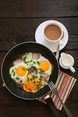 Fried eggs with bacon in a frying pan and coffee on a wooden table