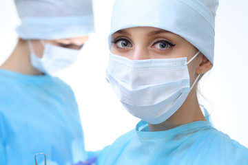 Close up of surgeon woman looking at camera while colleagues performing in background in operation room, isolated. Surgery and medicine concept