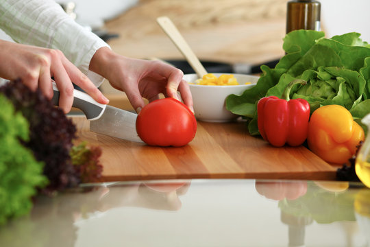 Closeup of human female hands cooking vegetables salad in kitchen on the glass table with reflection. Healthy meal and vegetarian concept