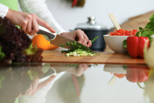 Closeup of human female hands cooking vegetables salad in kitchen on the glass table with reflection. Healthy meal and vegetarian concept