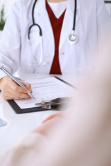 Close up of a female doctor filling up  an application form while sitting at the table. Medicine and health care concept