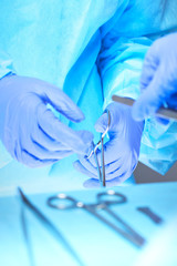 Close-up of of surgeons hands at work in operating theater toned in blue. Medical team performing operation