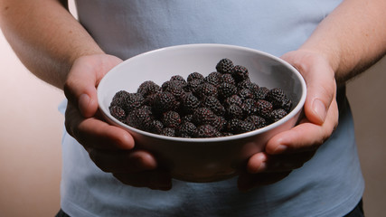 Man holds a dish with a blackberries at hands