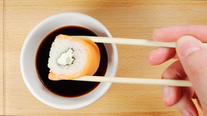 TOP VIEW: Human hand dips a sushi by chopsticks in a soy sauce cup