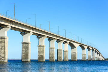Concrete bridge over water. Gray pillars support the weight of the structure. Vital part of infrastructure and link the island of Oland to mainland Sweden. - 141015825