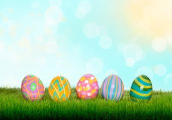 Fototapeta na wymiar Colourful painted Easter Eggs on green grass and blurred garden and blue sky background.