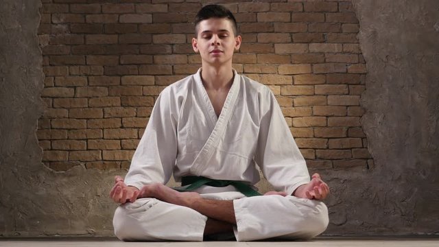 An eighteen year old sportsman in a karate kimono sits in Lotus pose