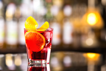 Closeup glass od red alcoholic cocktail decorated with lemon at bright bar stand background.