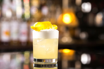 Closeup glass of whiskey sour cocktail decorated with lemon at bar background.