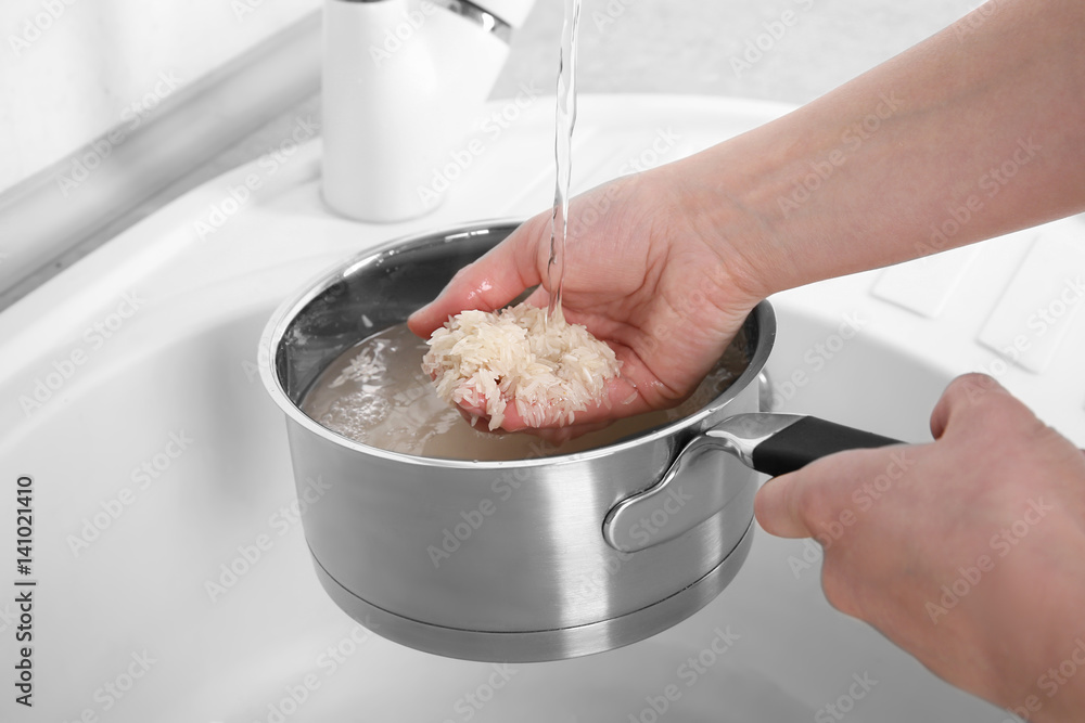 Canvas Prints Woman rinsing rice in saucepan under running water