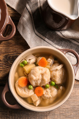Ceramic pan with delicious chicken and dumplings on wooden kitchen table