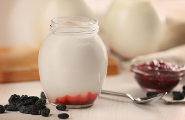 Glass jar with tasty yogurt and jam on white wooden background