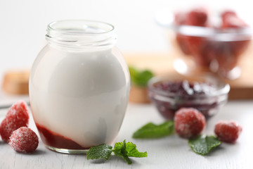 Glass jar with tasty yogurt and jam on  wooden background