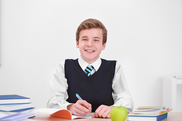 Cute schoolboy writing in notebook while sitting at table