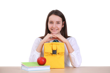 Cute schoolgirl with lunch bag sitting at table in classroom