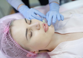 Fototapeta na wymiar Hands of cosmetologist making injection in face, lips. Young woman gets beauty facial injections in salon. Face aging, rejuvenation and hydration procedures. Aesthetic cosmetology. Close up.