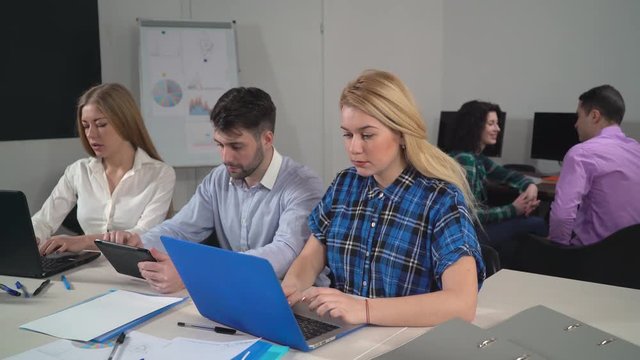 friends watching funny photo their coworker. Young creative people in office talking and laughing sitting at the working place. business team have fun wearing in casual clothes.