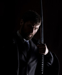 stern angry businessman in a wool coat with sword in dark background