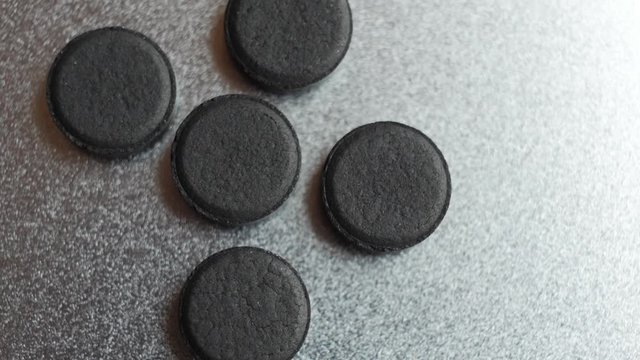 Closed up Activated charcoal carbon pills turning on a metal background. Top view., slow motion.