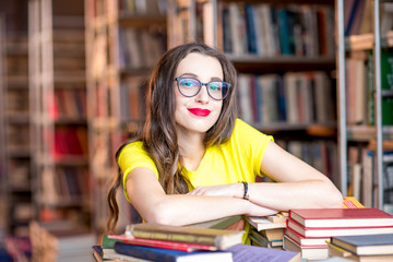 Portrait of young enthusiastic female student studying with a lot of books at the library